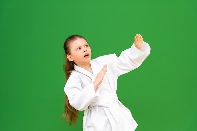 Una niña pequeña con un kimono blanco hace un calentamiento antes de entrenar en un niño de fondo verde que está estudiando artes marciales