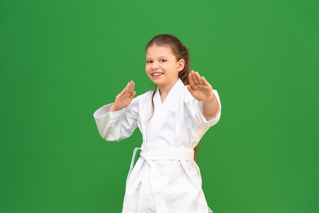 Una niña pequeña con un kimono blanco hace un calentamiento antes de entrenar en un niño de fondo verde que está estudiando artes marciales