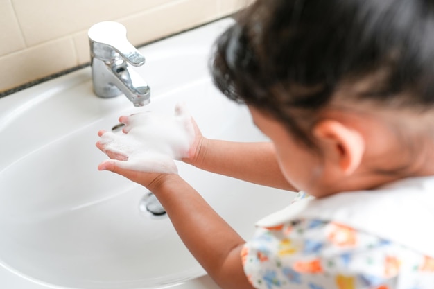 Niña pequeña lavándose las manos para prevenir virus, bacterias y gérmenes en el fregadero