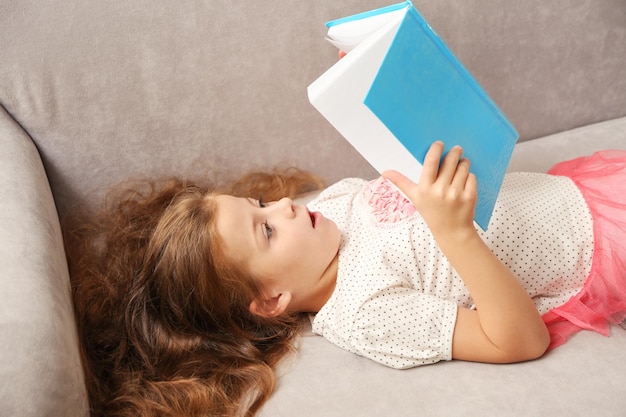 Niña pequeña leyendo un libro en el sofá