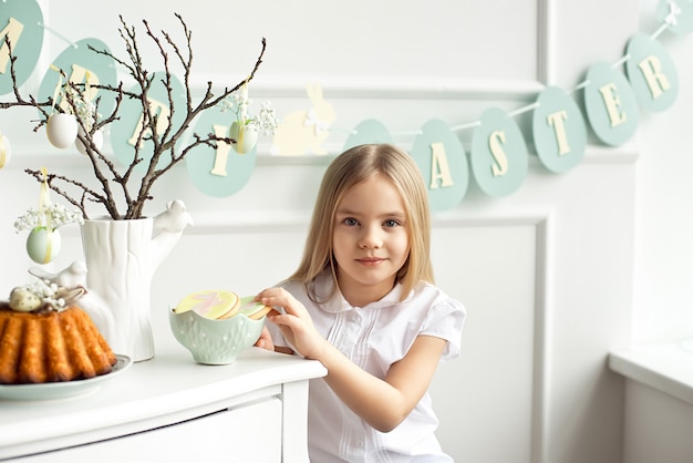 Foto la niña pequeña linda en una camisa blanca está comiendo las galletas