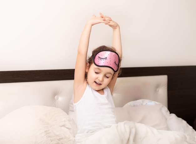 Foto una niña pequeña y linda se despierta por la mañana estirando la mano y sube al aire mientras está sentada en la cama