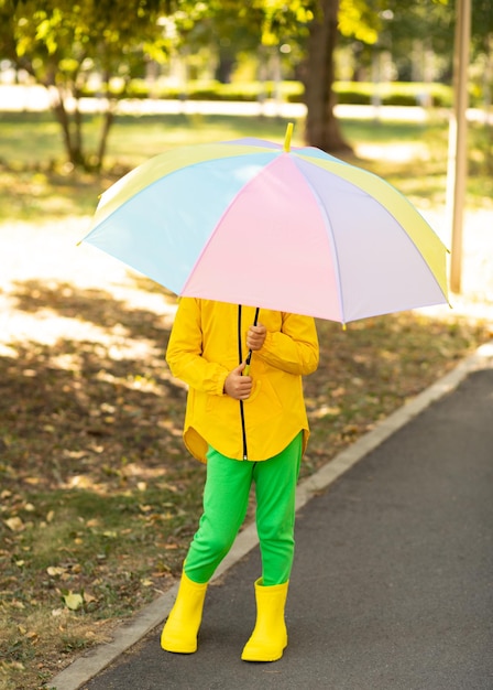 Niña pequeña y linda con un impermeable amarillo con un paraguas arcoíris multicolor