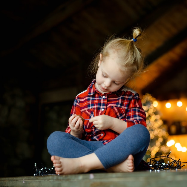 Niña pequeña linda que come el huevo de chocolate que se sienta en una casa de caza adornada para la Navidad. El concepto de una mañana de navidad. De cerca el retrato