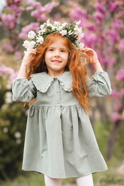 Una niña pequeña y linda que se ríe de 3 a 4 años usa una corona floral y un elegante vestido rústico sobre la naturaleza