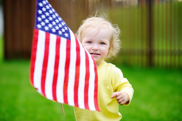 Niña pequeña linda que sostiene la bandera americana.