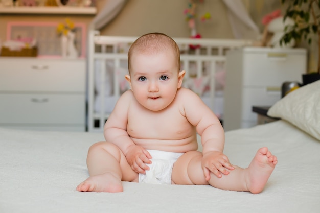 La niña pequeña linda sonríe en pañales que se sientan en cama en casa