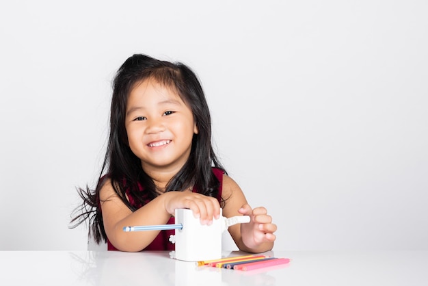 Niña pequeña y linda sonríe usando sacapuntas mientras hace la tarea en