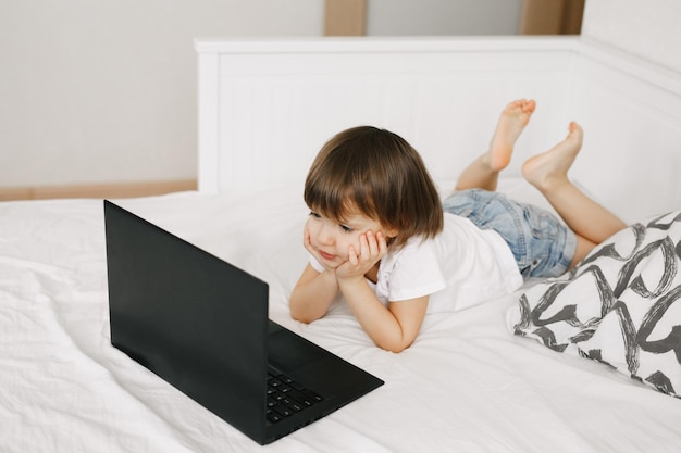 Niña pequeña y linda usando una laptop en la cama en casa