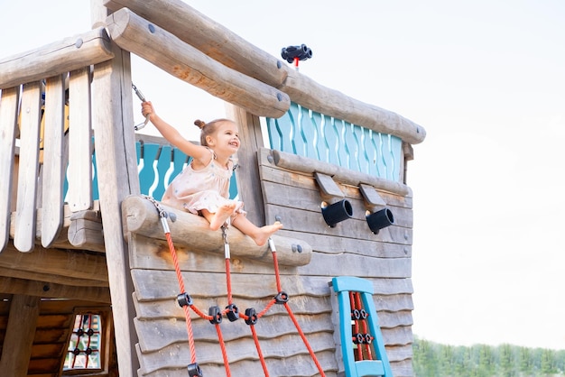 niña pequeña y linda vestida jugando en el patio de juegos para niños en el día de verano