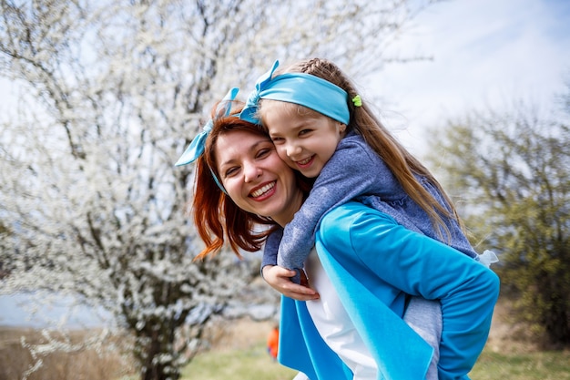 Niña pequeña y madre mujer camina por el bosque de primavera con árboles en flor, reír y jugar, el comienzo de la primavera, vacaciones familiares, amor de los padres