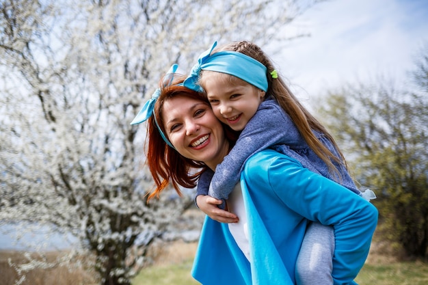 Niña pequeña y madre mujer camina por el bosque de primavera con árboles en flor, reír y jugar, el comienzo de la primavera, vacaciones familiares, amor de los padres