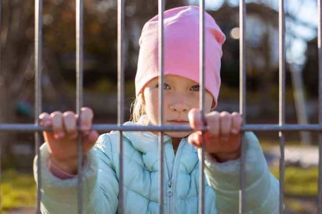 Foto niña pequeña mira a través de la valla de hierro en la calle