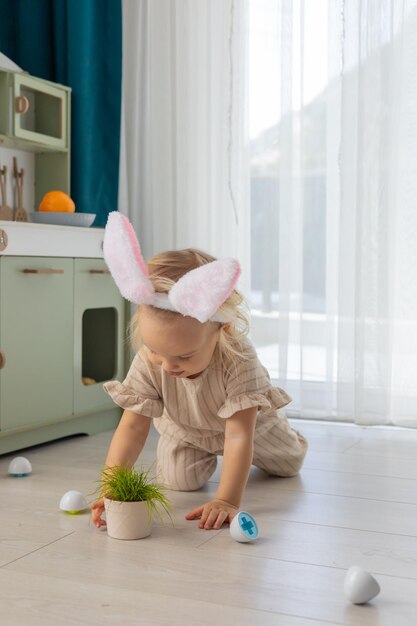 Una niña pequeña con orejas de conejo rosas juega con huevos de monetsori de juguete