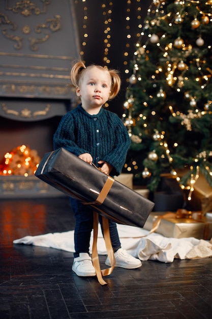 Niña pequeña parada cerca del árbol de Navidad con un regalo