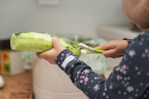 Niña pequeña pelando pepino con un pelador