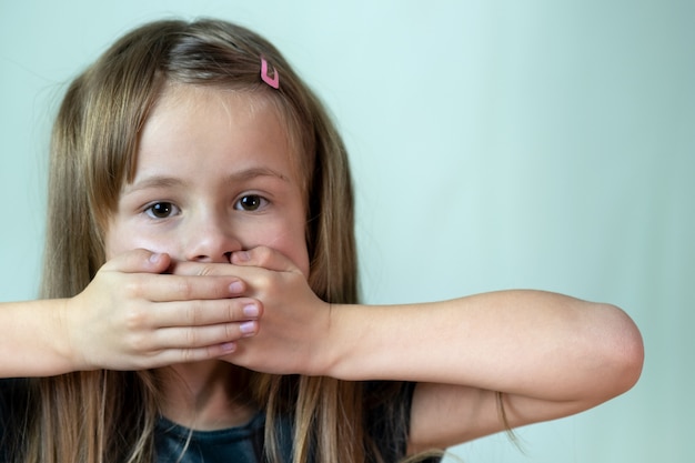 Niña pequeña con el pelo largo cubriendo su boca con las manos