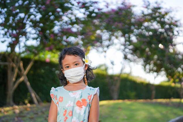 Niña pequeña de pie en el campo con mascarilla protectora