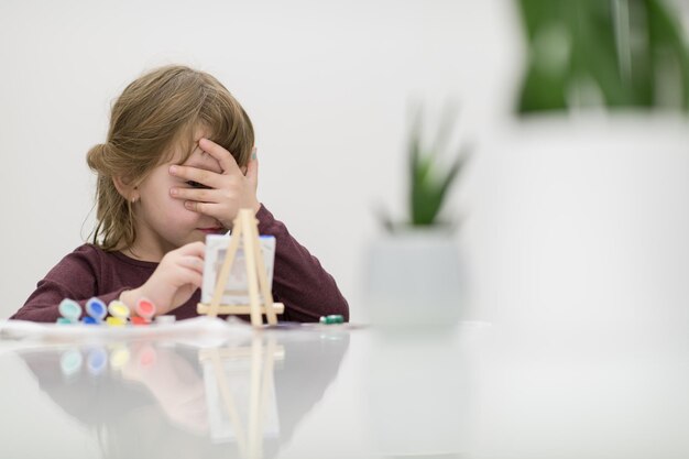 niña pequeña pintando una imagen de lienzo en casa mientras oculta la cara