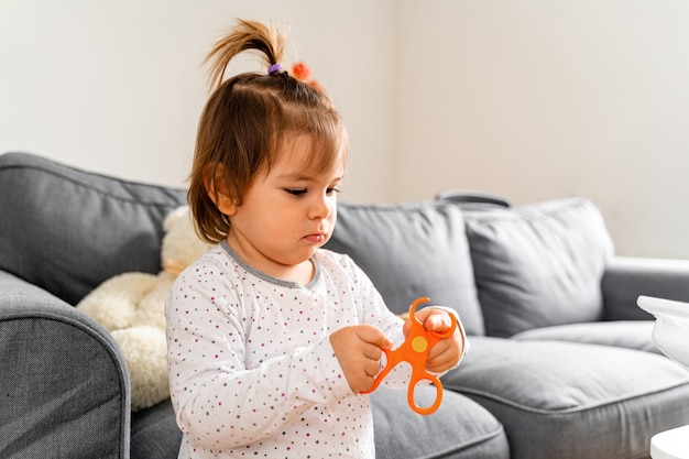 Niña pequeña que juega con las tijeras plásticas del juguete en casa