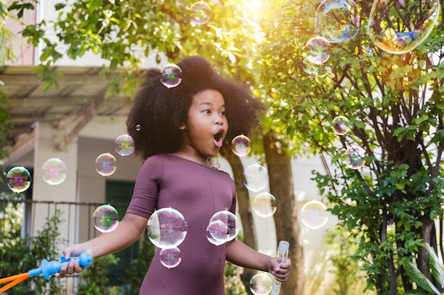 Niña pequeña que sopla pompas de jabón en el parque de verano Actividad al aire libre