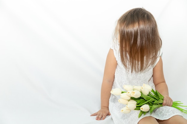 Niña pequeña con un ramo de tulipanes con un vestido blanco mira a un lado una sonrisa amable