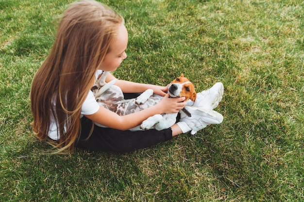 Una niña pequeña rasca el vientre de su perro Jack Russell Terrier Un perro feliz está acostado sobre la hierba verde en el parque una mascota