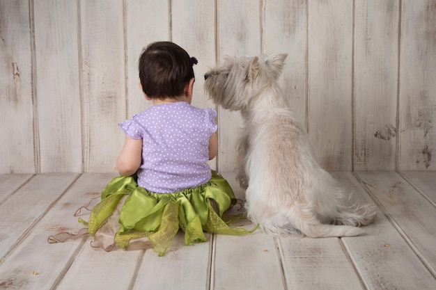 Foto niña pequeña sentada hacia atrás junto a un pequeño perro blanco west highland white terrier westie