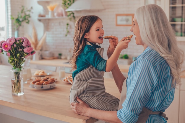 Foto niña pequeña sentada en la mesa de la cocina y alimentando a la abuela con galletas