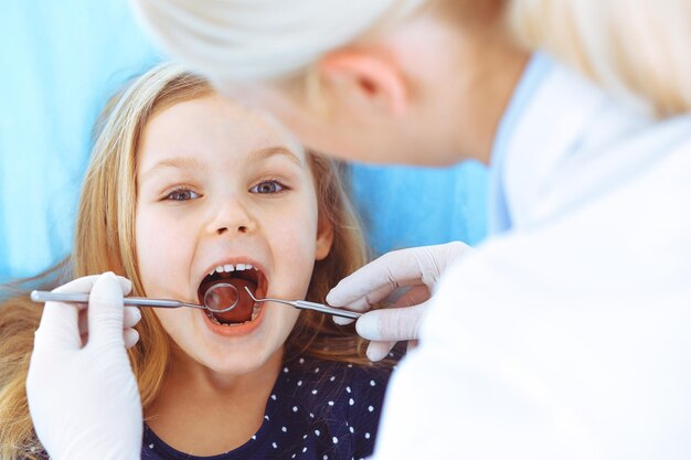 Niña pequeña sentada en el sillón dental con la boca abierta durante el chequeo oral mientras el médico. Visitando la oficina del dentista. Concepto de medicina. foto tonificada.