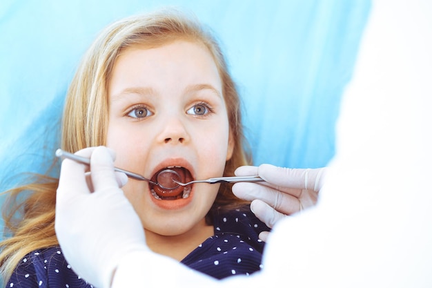 Niña pequeña sentada en el sillón dental con la boca abierta durante el chequeo oral mientras el médico. Visitando la oficina del dentista. Concepto de medicina. foto tonificada.