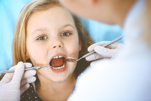 Niña pequeña sentada en el sillón dental con la boca abierta durante el chequeo oral mientras el médico. Visitando la oficina del dentista. Concepto de medicina. foto tonificada.