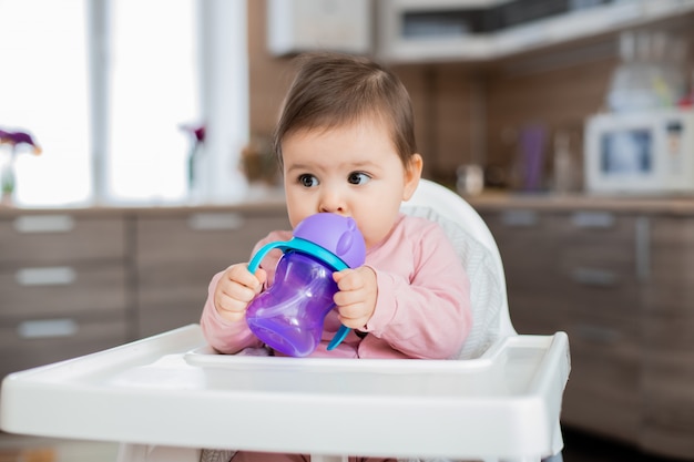 La niña pequeña se sienta en la silla de un niño en la cocina