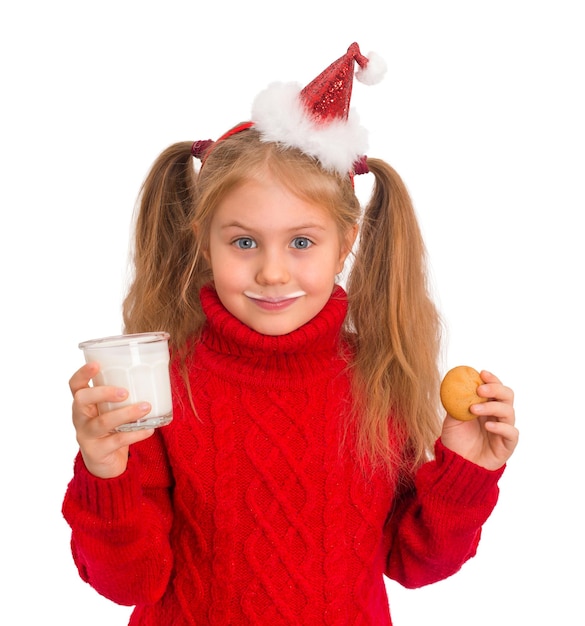 Niña pequeña con sombrero de santa con vaso de leche y galletas aisladas Chica bebe leche en Navidad