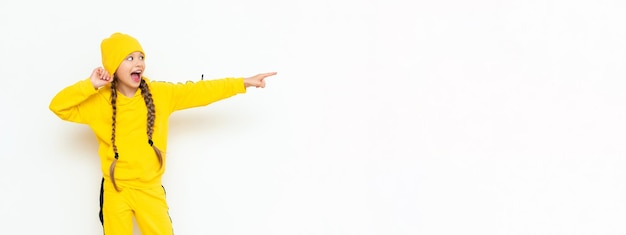 Una niña pequeña con un sombrero y un traje amarillo apunta a su anuncio en un fondo blanco aislado Ropa de otoño para niños Espacio de copia