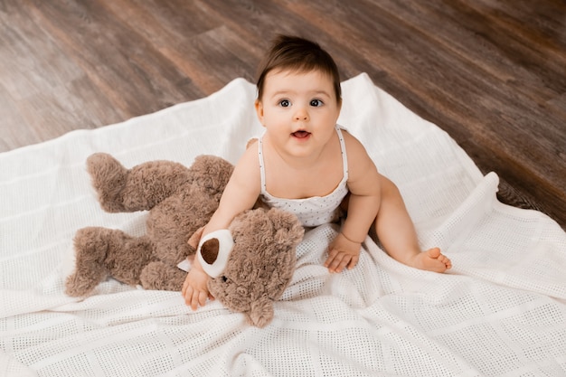 La niña pequeña sonríe sentado en el piso de madera con osito de peluche