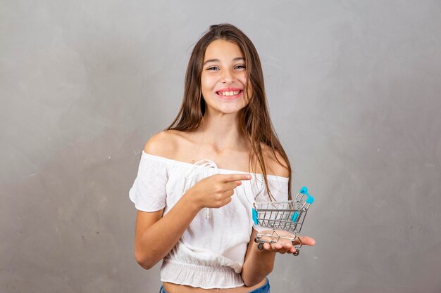 Foto niña pequeña sosteniendo un carrito de compras en miniatura sobre fondo gris con espacio libre para texto concepto de compras y comercio electrónico