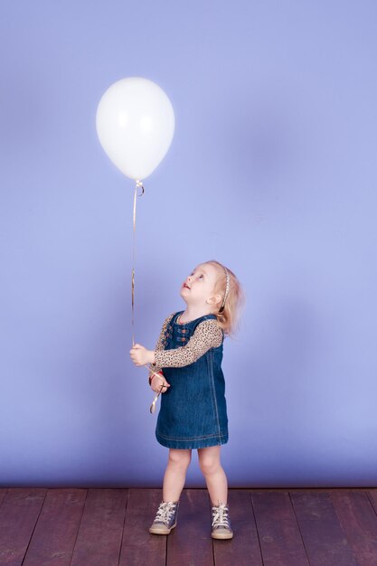 Niña pequeña sosteniendo globo usa ropa de moda sobre azul interior