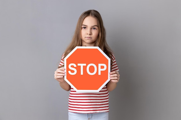 Niña pequeña sosteniendo una señal de stop roja mirando a la cámara con una seria prohibición de expresiones faciales