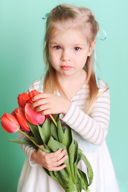 Niña pequeña sosteniendo tulipanes rojos con vestido elegante mirando a la cámara