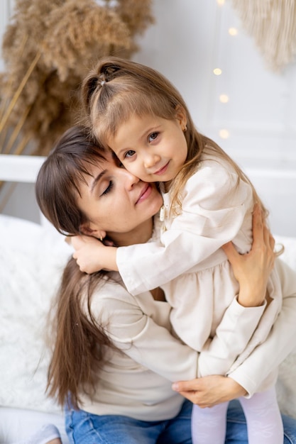 Una niña pequeña con su madre abrazándose y besándose en casa en la cama Estilo de vida Familia feliz y maternidad Día Internacional de la Mujer o Día de la Madre Fotografía de alta calidad