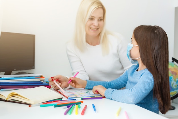 Una niña pequeña con su madre están haciendo ejercicios en el cuaderno a distancia, educación en casa, cuarentena