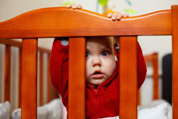 Niña pequeña con un suéter rojo, sonríe maravillosamente, en una cuna, juega y se divierte, foto emocional