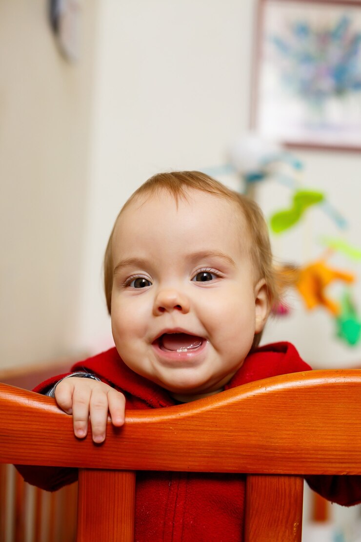 Niña pequeña con un suéter rojo, sonríe maravillosamente, en una cuna, juega y se divierte, foto emocional