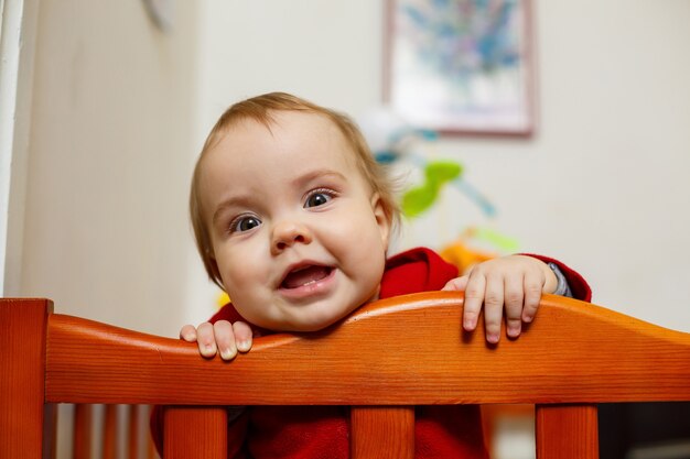 Niña pequeña con un suéter rojo, sonríe maravillosamente, en una cuna, juega y se divierte, foto emocional