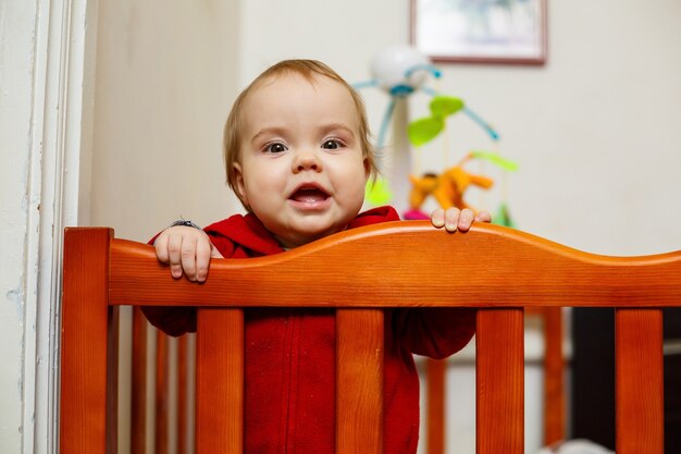 Niña pequeña con un suéter rojo, sonríe maravillosamente, en una cuna, juega y se divierte, foto emocional