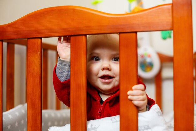 Niña pequeña con un suéter rojo, sonríe maravillosamente, en una cuna, juega y se divierte, foto emocional