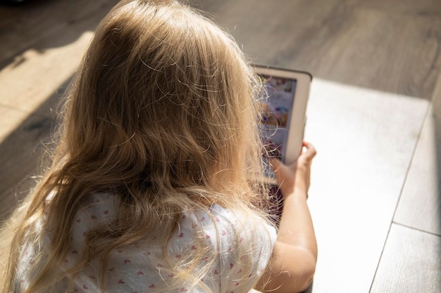 Foto niña pequeña tendida en el suelo mirando la tableta