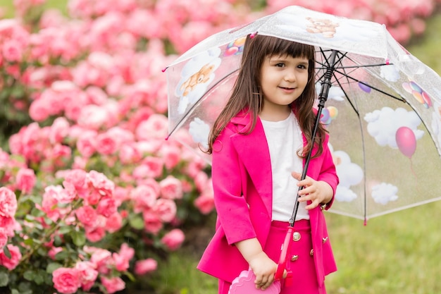 Una niña pequeña con un traje fucsia brillante camina afuera bajo una pancarta de tarjeta de paraguas transparente