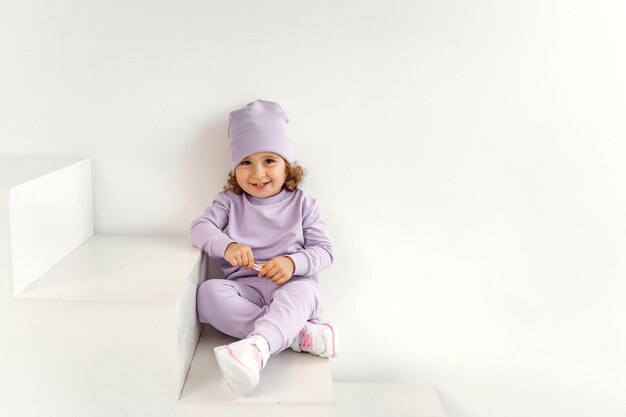 Una niña pequeña con un traje morado y un sombrero sobre un fondo claro está jugando